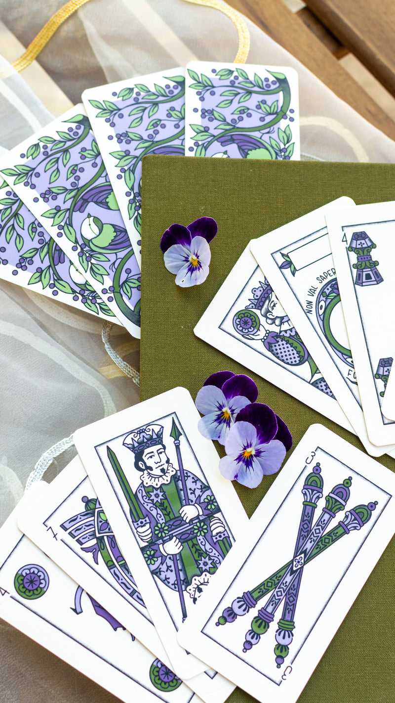 Carte con le viole disegnate, sparse accanto alla loro scatola verde oliva e a viole vere