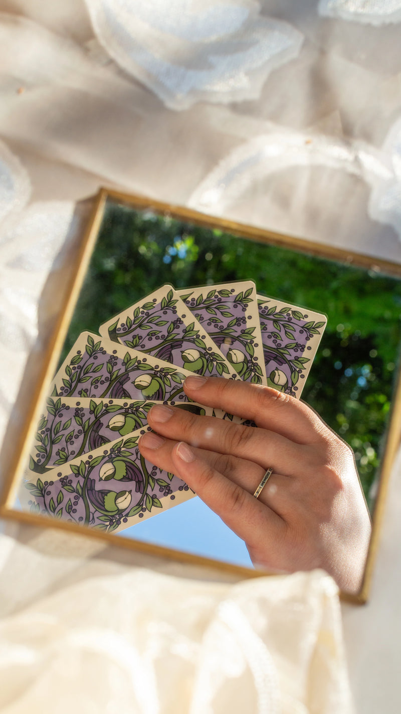 Mazzi di carte in piedi accanto a un bouquet di fiori secchi, su una tavola apparecchiata di bianco